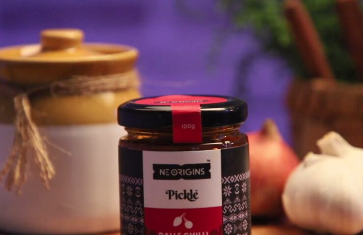 NE Origins Dalle Chilli Pickle jar with garlic and an earthen pot on a rustic table